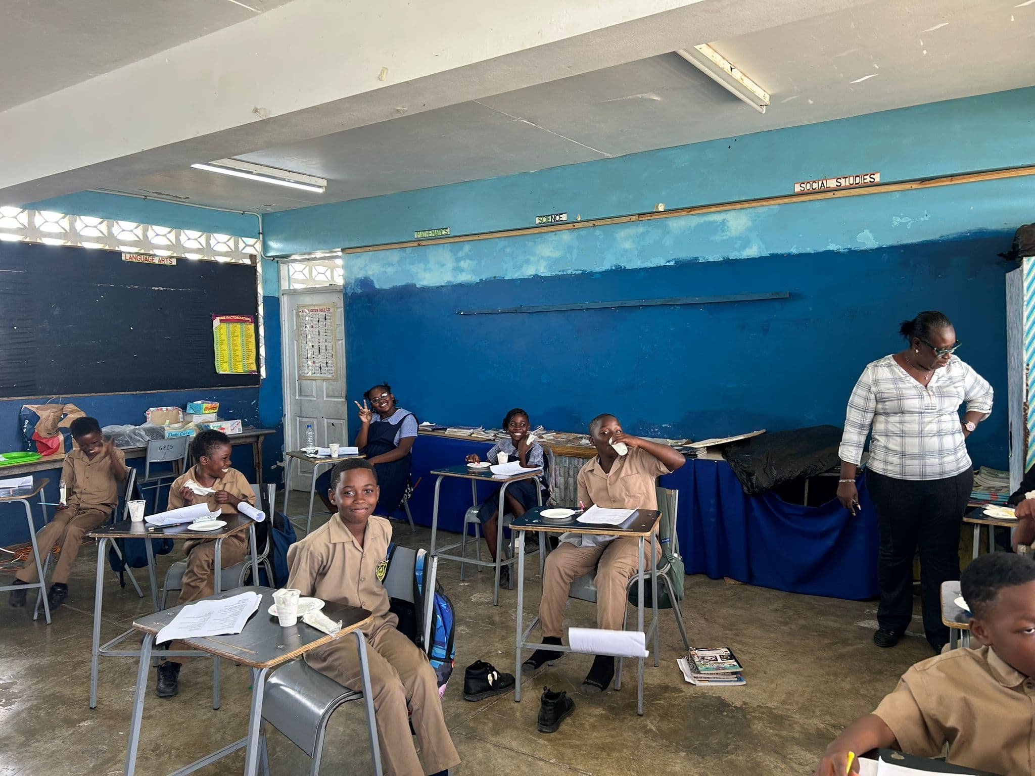 A teacher walks between desks while students in tan uniforms hold up their ice cream cups.