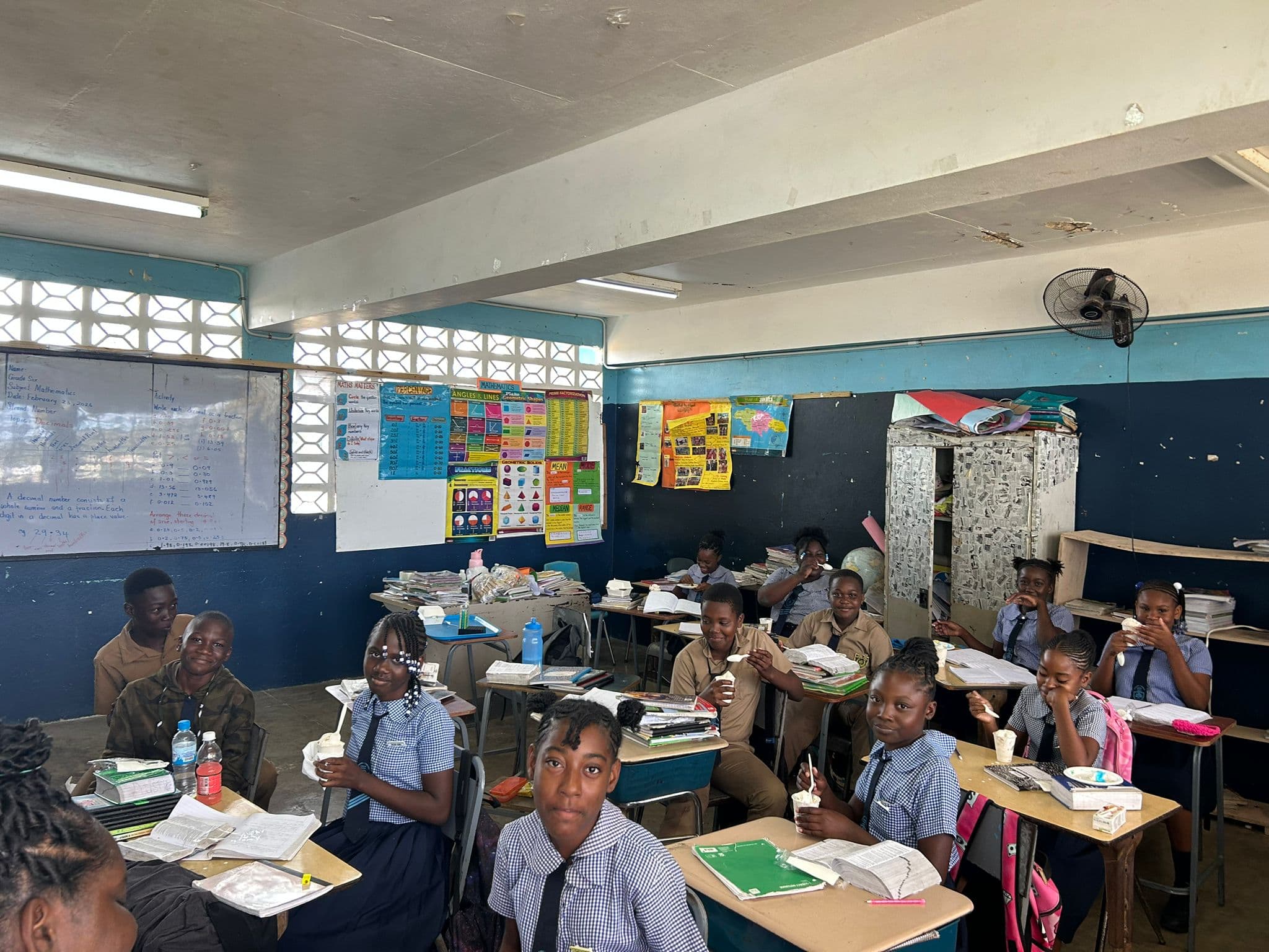Rows of students in navy-and-white uniforms with ice cream cups; a world map is visible on the back wall.