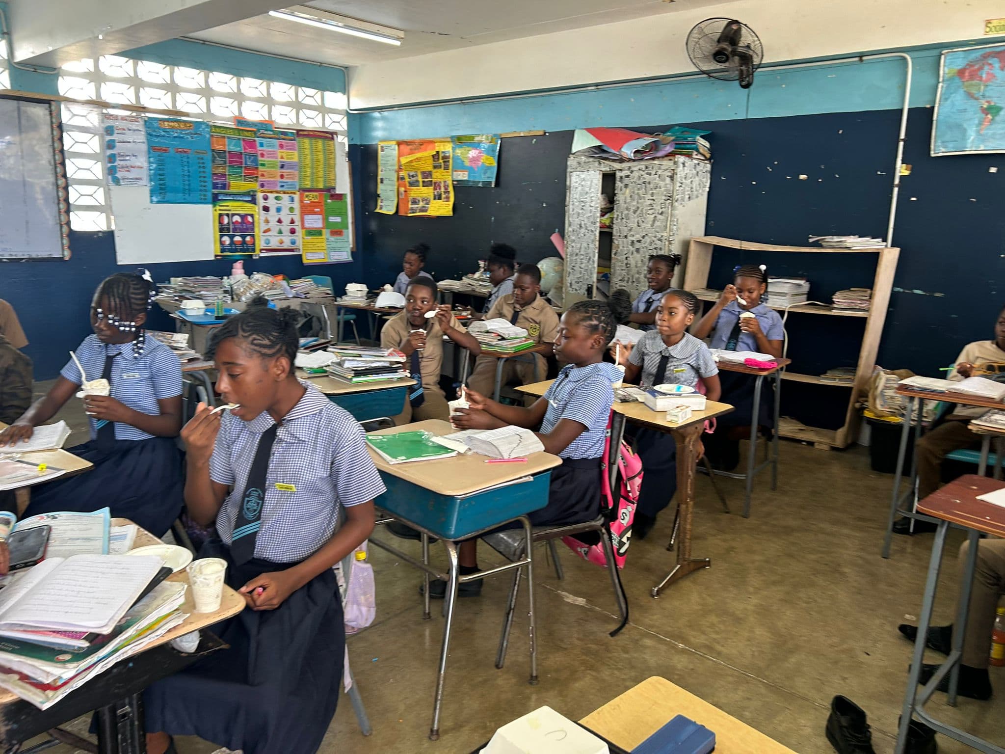 A group of students eating ice cream at their desks, with books and backpacks beside them.