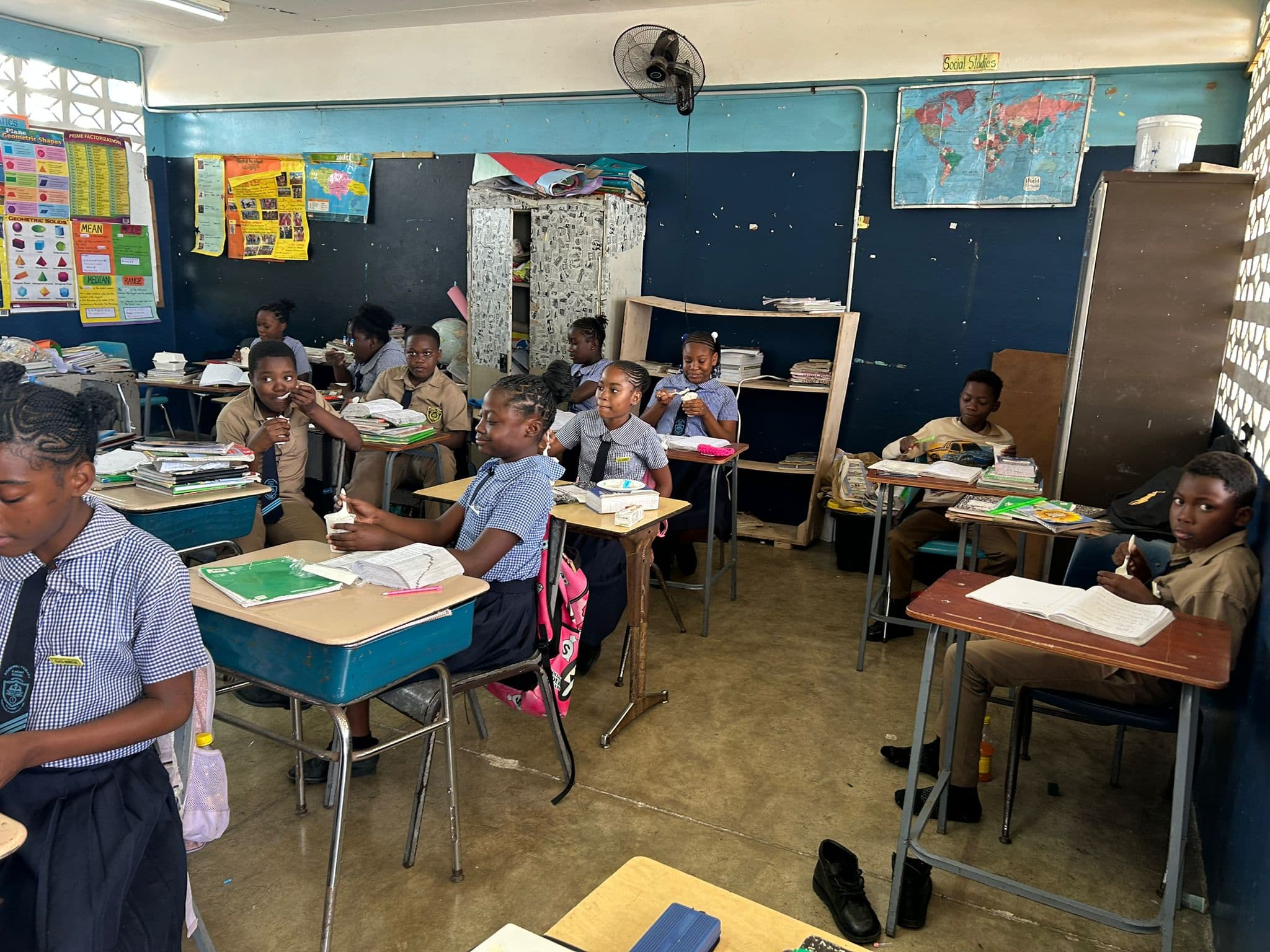 Students in white and navy uniforms seated at desk pods, spoons raised, enjoying their ice cream.