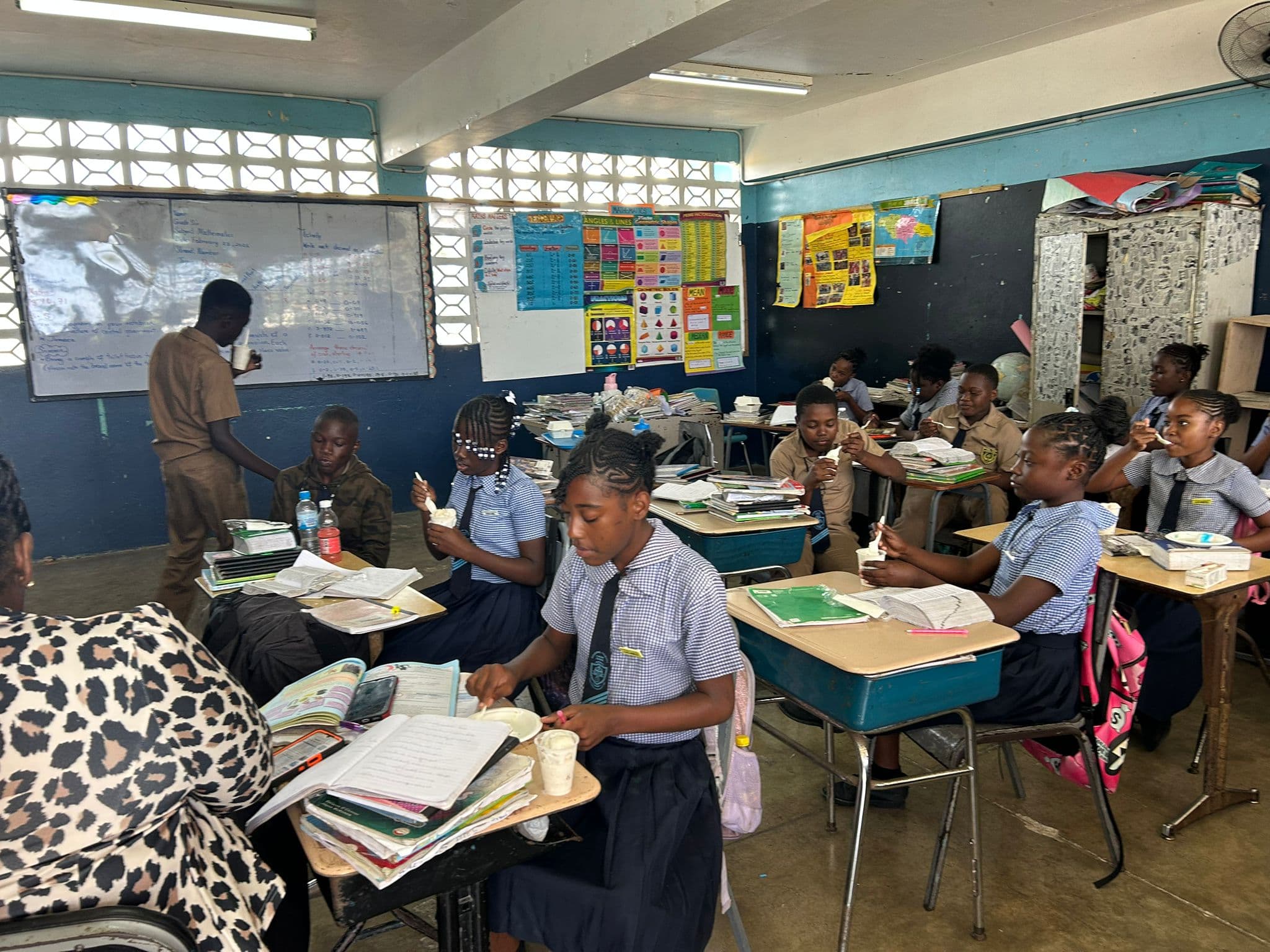 A teacher at the front of the classroom while students in navy-and-white uniforms eat ice cream at their desks.