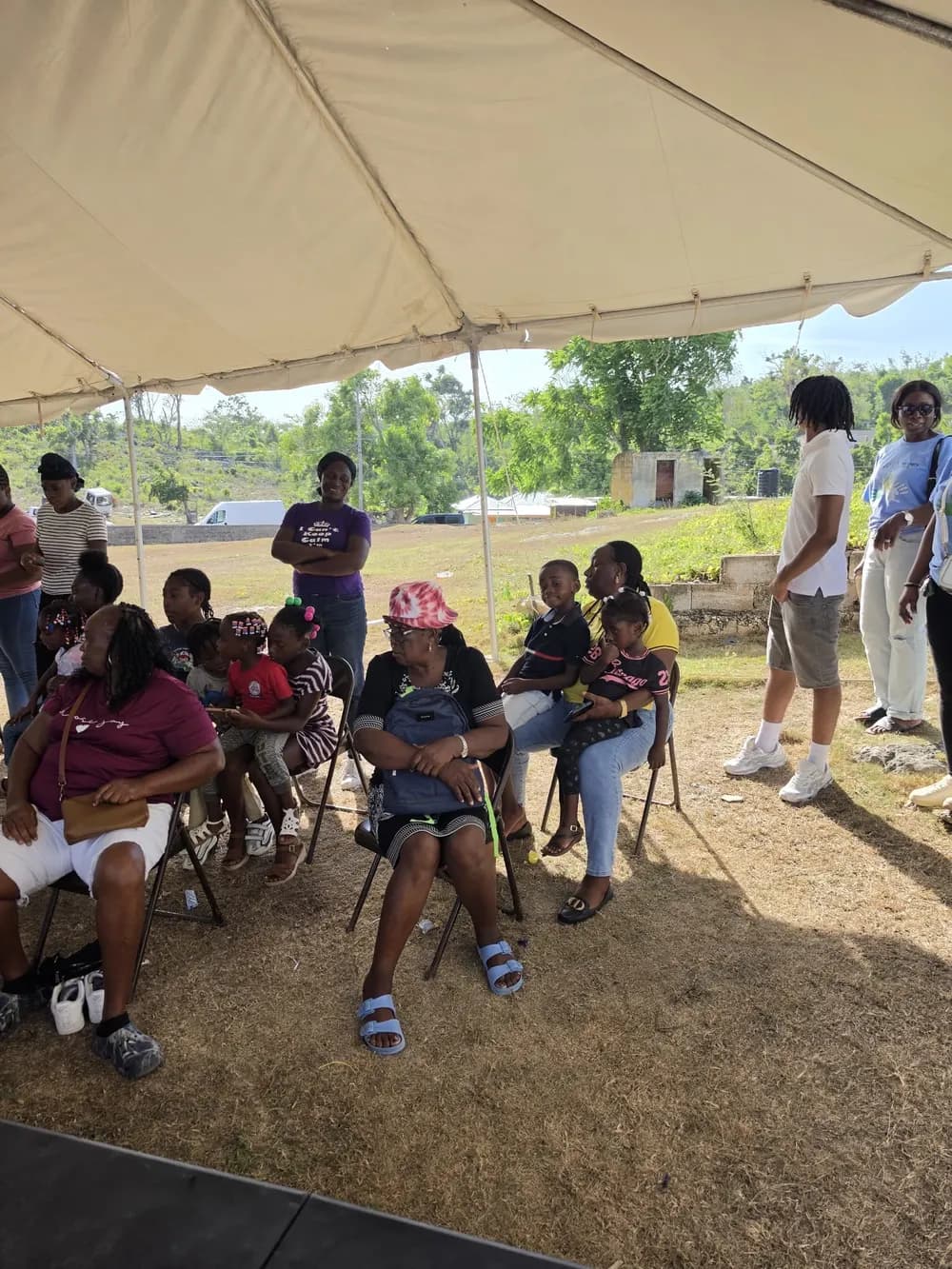 Families and children seated beneath a tent at the community gathering